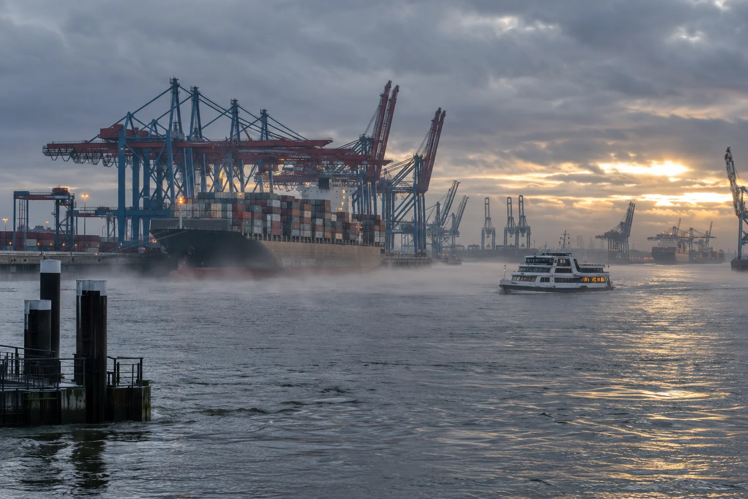 Container ships and cranes in the port of Hamburg on a grey winter morning, seen across the Elbe.
