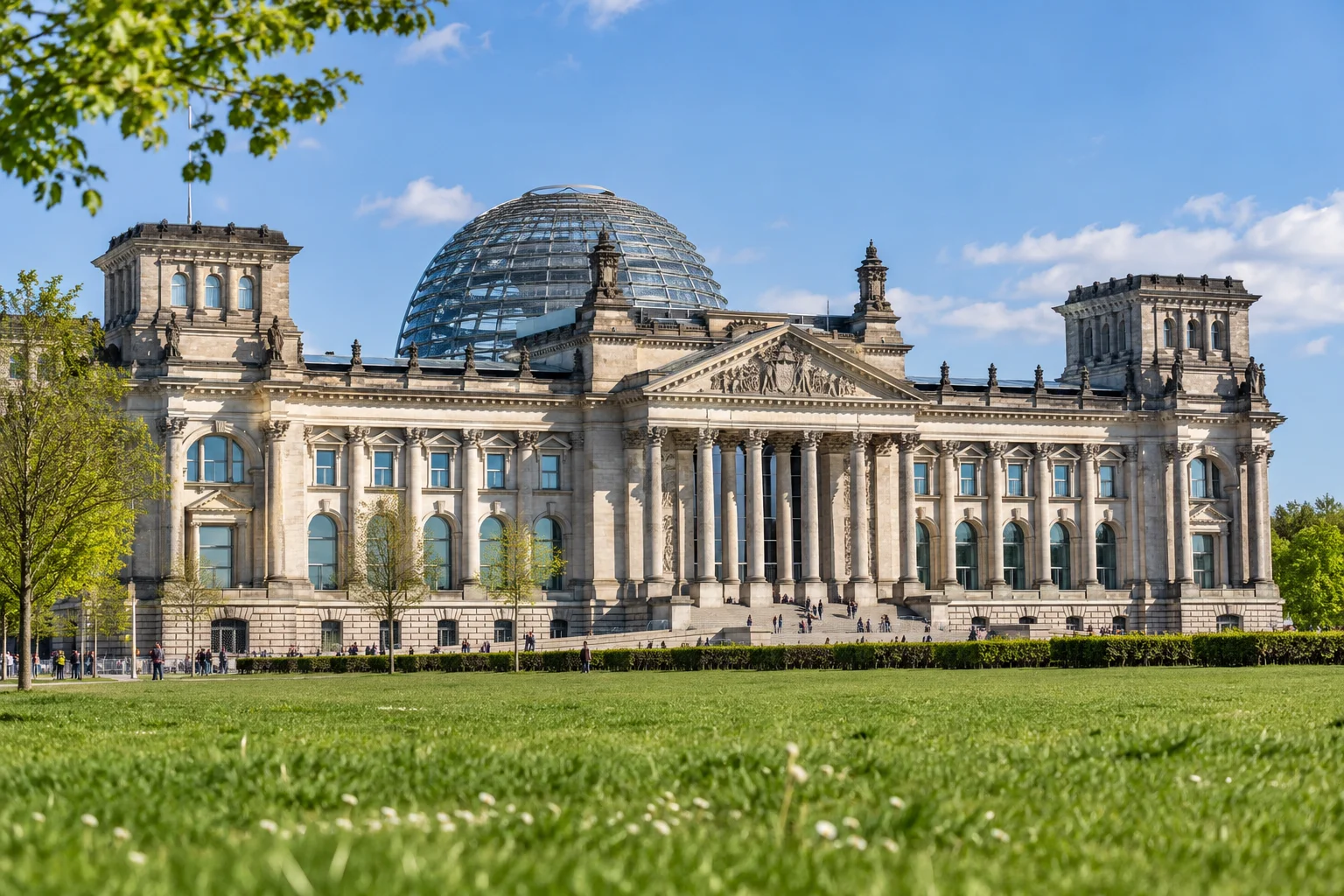 The glass dome of the Reichstag building in Berlin seen from the lawn on a bright spring morning, a few people walking in the distance.